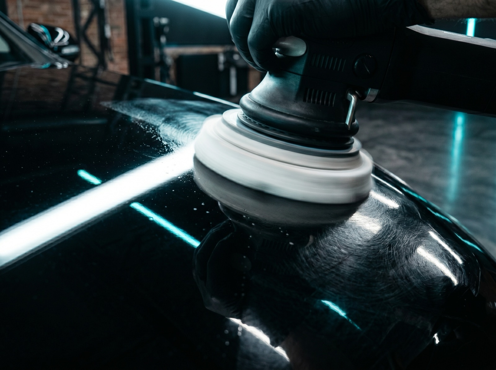 Dual-action polisher refining black car paint to a mirror finish under an LED inspection light